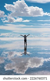 Young man in his twenties, surrounded by the vast expanse of the Uyuni Salt Flats in Bolivia, the salt flats have been transformed by the recent rainfall, creating a mesmerizing mirror-like reflection