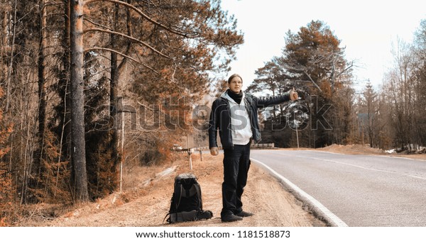 A young man is hitchhiking around\
the country. The man is trying to catch a passing car for\
traveling. The man with the backpack went hitchhiking to\
south.\

