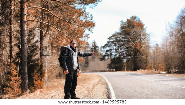 A young man is hitchhiking around\
the country. The man is trying to catch a passing car for\
traveling. The man with the backpack went hitchhiking to\
south.\
