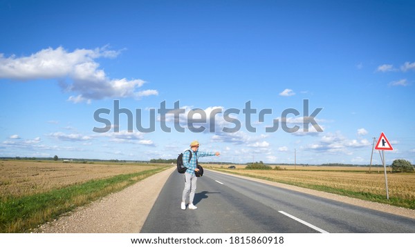 A young man is hitchhiking around\
the country. The man is trying to catch a passing car for\
traveling. The man with the backpack went hitchhiking to\
south.