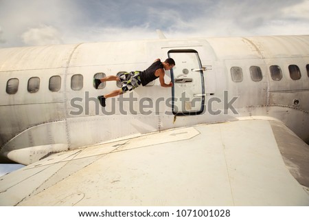 Young man holding airplane door from outside and hangs in the air. Aircraft crash, extreme flight