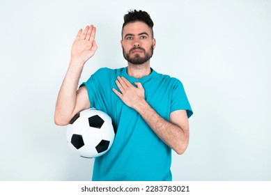 Young man holding a ball over white background Swearing with hand on chest and open palm, making a loyalty promise oath - Powered by Shutterstock