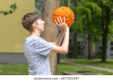 young man holding a basketball in his hands, looking up at it with a surprised expression.  typical urban setting. Boy relaxed stance and the presence of the basketball - Powered by Shutterstock