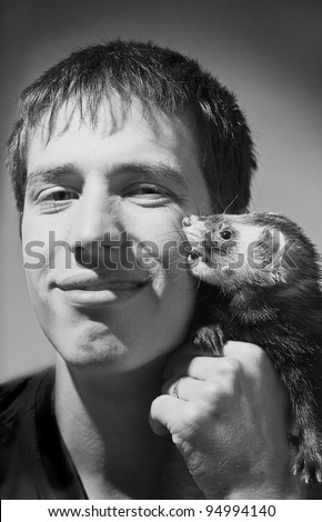 Young man holding beautiful ferret who bites his cheek