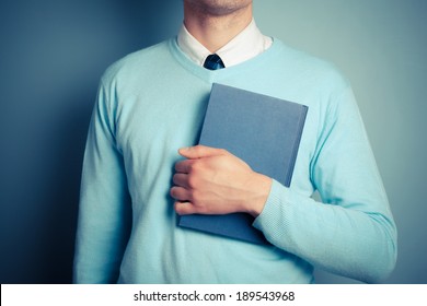 A Young Man Is Holding A Big Blue Book