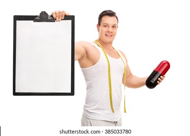 Young man holding a big diet pill and a clipboard with a blank sheet on it isolated on white background