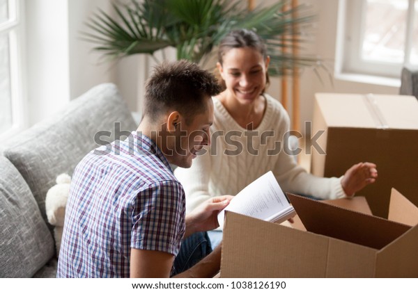 Young man holding book helping wife to pack cardboard boxes on moving