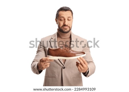 Young man holding a brown leather shoe and looking at it isolated on white background