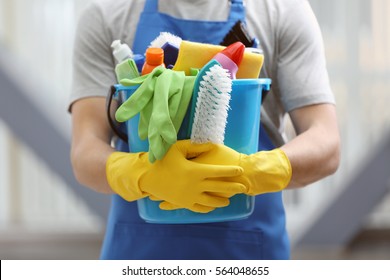 Young man holding bucket with cleaning equipment and supplies indoors, closeup