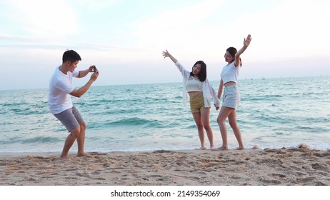 Young man holding camera taking photo of teenage girls posing on beach in summer, group of friends having fun taking a picture together on the beach at sunset, keep special memories of friendship. - Powered by Shutterstock