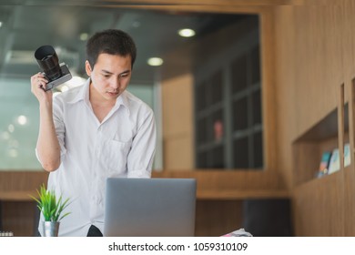 Young man holding a camera and using laptop.	