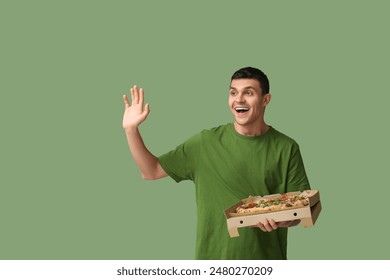 Young man holding cardboard box with tasty pizza on green background - Powered by Shutterstock