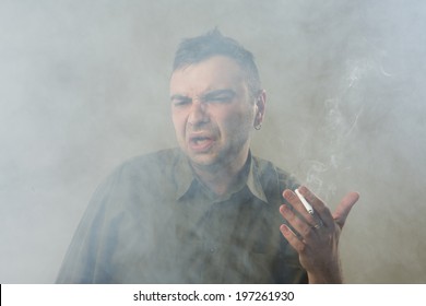 Young man holding cigarette aversion smoking badly. Suffocating. Quit and give up smoking. Space in the cigarette smoke.  smoking kills. Gray background. Studio shot.