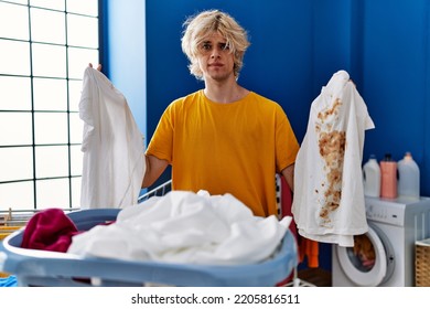 Young Man Holding Clean White T Shirt And T Shirt With Dirty Stain Skeptic And Nervous, Frowning Upset Because Of Problem. Negative Person. 