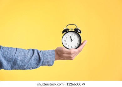 Young man holding clock on color background. Time management