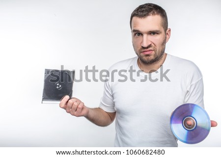 Young man holding a compact disk in one hand and a box from it in another hand and staring at camera. Time goes so fast that now he doesn't know what to do with this disk. Isolated on white background