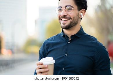 Young Man Holding A Cup Of Coffee While Walking Outdoors.