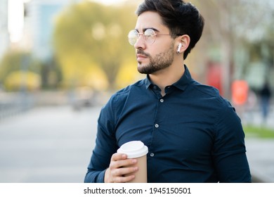 Young Man Holding A Cup Of Coffee While Walking Outdoors.