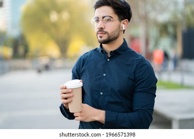 Young Man Holding A Cup Of Coffee While Walking Outdoors.