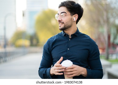 Young Man Holding A Cup Of Coffee While Walking Outdoors.