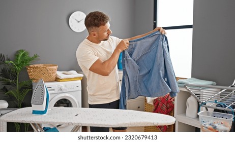 Joven sosteniendo planchado de camiseta de denim en la lavandería