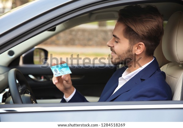 Young man holding\
driving license in car