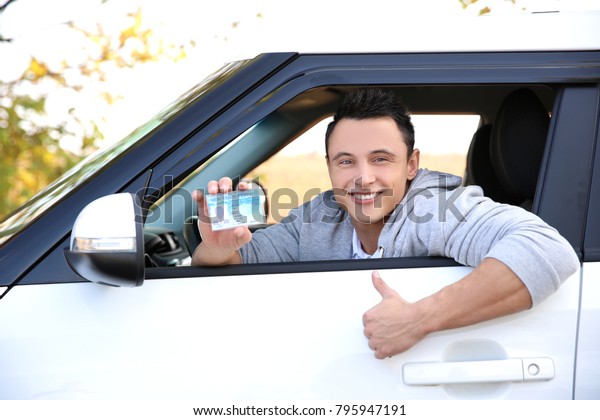 Young man holding\
driving license in car