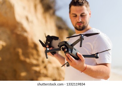 Young man holding drone before flight near ocean or sea. Pretty guy prepare to pilot outdoor