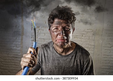 young man holding electrical cable smoking after domestic accident with dirty burnt face in funny sad expression in electricity DIY repairs danger concept  in black smoke background