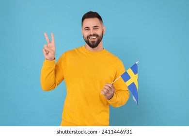 Young man holding flag of Sweden on light blue background