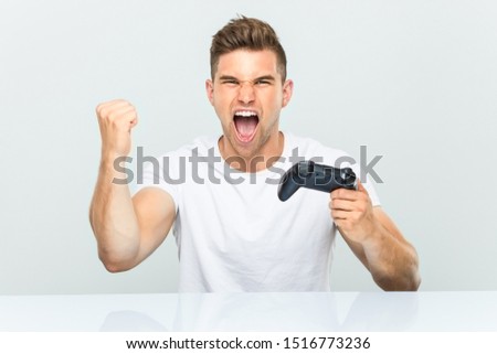Young man holding a game controller cheering carefree and excited. Victory concept.