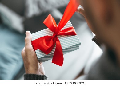 Young Man Holding Gift With Red Ribbon. Closeup. Opening Gift. 