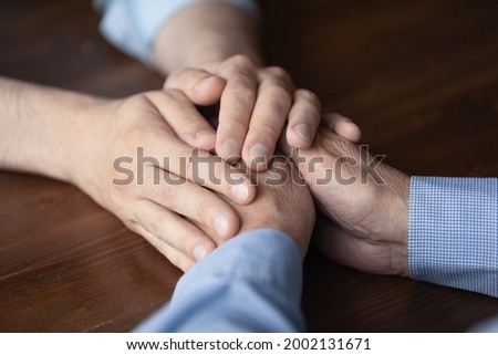 Young man holding hands of elderly father close up. Grown son giving comfort and support to senior father at moment of stress, grief, despair, disease. Family, empathy concept. Cropped shot