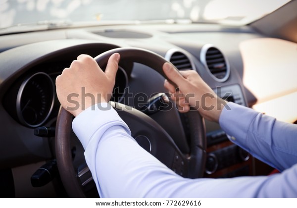 Young man\
holding hands on steering wheel of\
car
