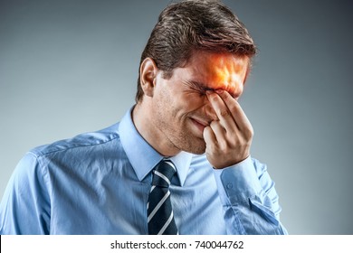 Young man holding his head in pain. Photo of man in shirt and tie grimacing in pain on gray background. Medical concept