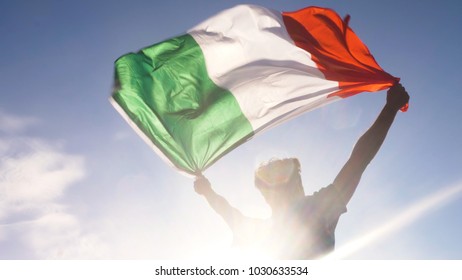 Young Man Holding Italian National Flag To The Sky With Two Hands At The Beach At Sunset