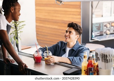 Young man holding juice on a counter of food truck looking at saleswoman - Powered by Shutterstock