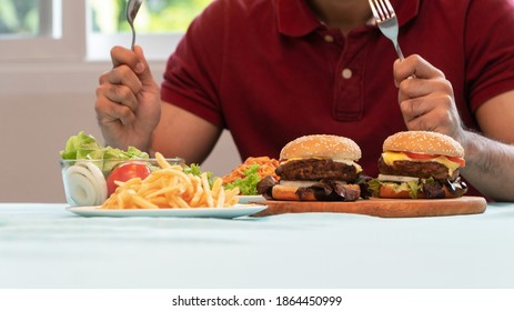 Young Man holding knife and fork are ready to eating a hamburger, French fries, and Spaghetti for Lunch. Concept of binge eating disorder (BED) and Relaxing with Eating junk food and unhealthy foods.