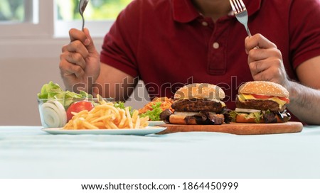 Young Man holding knife and fork are ready to eating a hamburger, French fries, and Spaghetti for Lunch. Concept of binge eating disorder (BED) and Relaxing with Eating junk food and unhealthy foods.