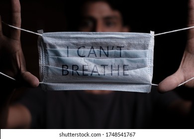 Young man holding medical mask with I Can't Breathe inscription on it. Cooncept of Protest about racial discrimination of Black People in U.S. America - Powered by Shutterstock