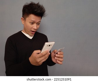 Young man holding mobile phone and credit card with shocked facial expression