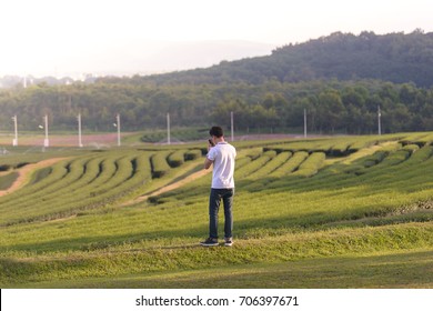 Young Man Holding Mobile Phone, Using Smartphone, Making A Call, Talking On The Phone, Standing On Tea Plantation