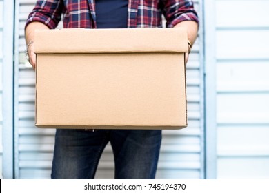 Young man holding a moving cardboard box in front of a storage door.Life style, storage, moving, storing, organizing concept. Space to write - Shutterstock ID 745194370