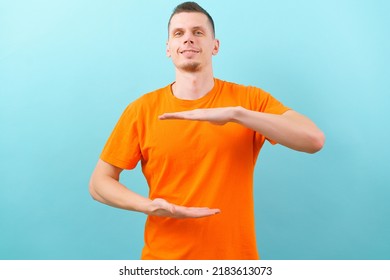 A young man holding an object with both hands in front of him, showing, offering, or advertising an object against a blue wall. Empty. Space. Concept. Object. Background. Portrait. Young. Copy