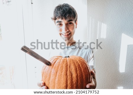 Young man holding on his hands a super textured pumpkin with a knife getting ready for halloween. Work and manual activities at home, party at home concept. Close up image funny happy image