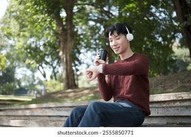 Young man holding paper cup and checking his smartwatch while sitting on outdoor stone steps. - Powered by Shutterstock