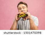 Young man holding a piece of hamburger. Bearded gyu eats fast food. Burger is not helpful food. Very hungry guy. Diet concept. Isolated over pink background.