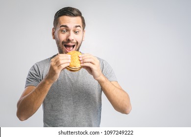 Young Man Holding A Piece Of Hamburger. Student Eats Fast Food. Burger Is Not Helpful Food. Very Hungry Guy. Diet Concept.