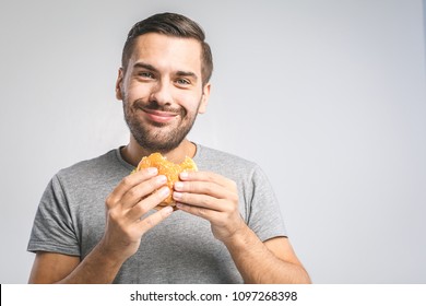 Young Man Holding A Piece Of Hamburger. Student Eats Fast Food. Burger Is Not Helpful Food. Very Hungry Guy. Diet Concept.