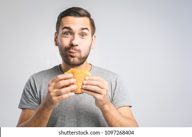 Young man holding a piece of hamburger. Student eats fast food. Burger is not helpful food. Very hungry guy. Diet concept.